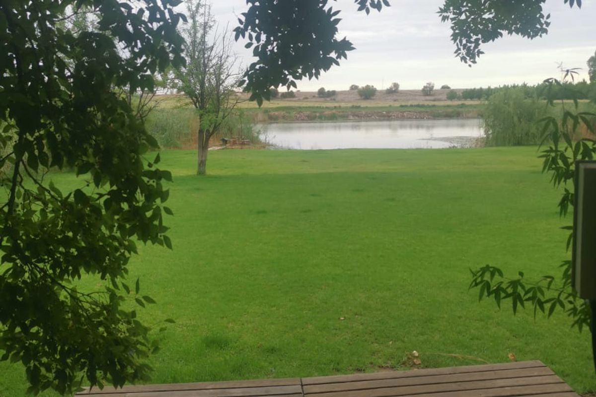 A scenic view of a well-maintained lawn and a tranquil pond, framed by overhanging tree branches.