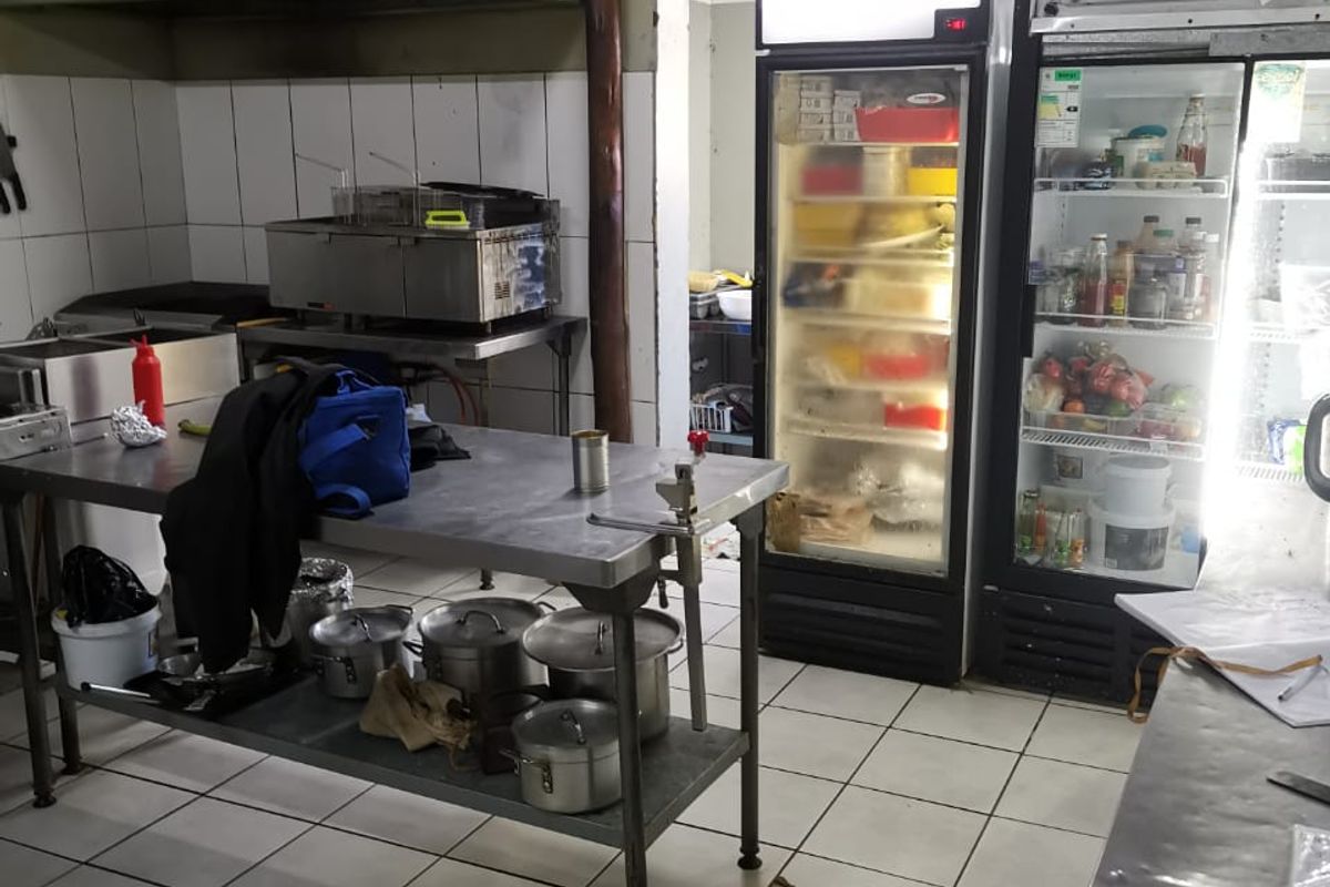 Commercial kitchen area featuring stainless steel prep surfaces, industrial refrigeration units, tiled flooring, and a traditional thatched roof structure.