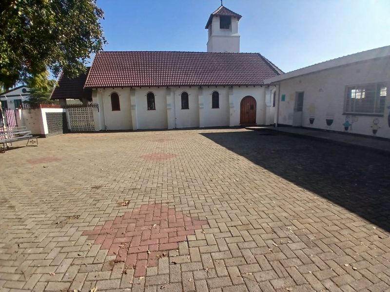 A paved courtyard area featuring a church-style building with a bell tower, arched windows, and a tiled roof.