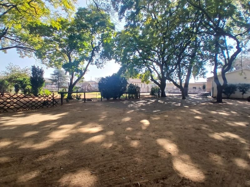A spacious outdoor garden area featuring mature trees, perimeter fencing, and a natural dirt ground surface.