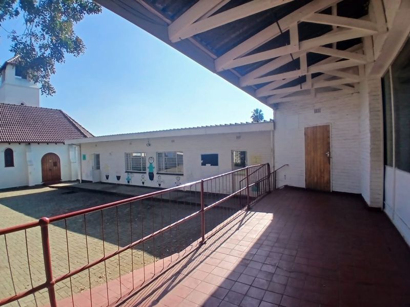 A covered outdoor patio area featuring tiled flooring, exposed timber roof trusses, and metal safety railings, overlooking a paved courtyard.