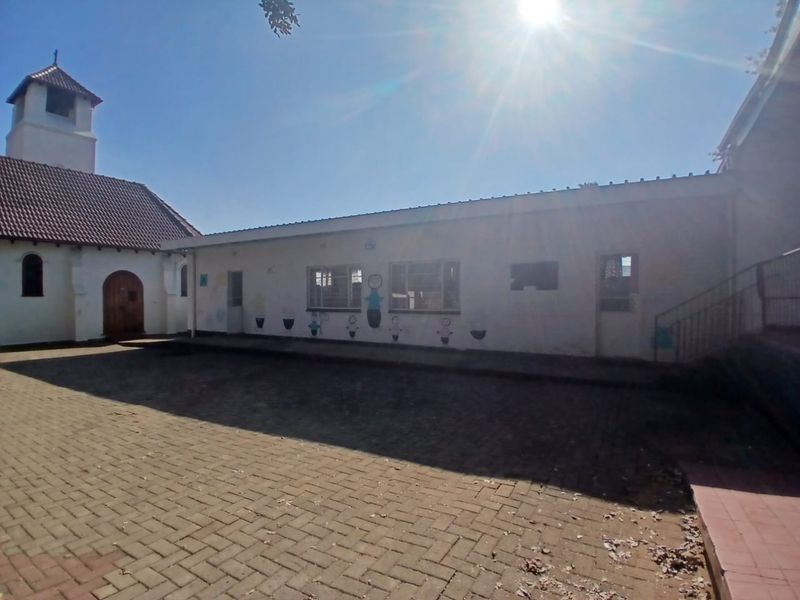 Exterior view of a commercial property courtyard featuring paved surfaces, a tiled roof structure, and adjacent building facade with casement windows.