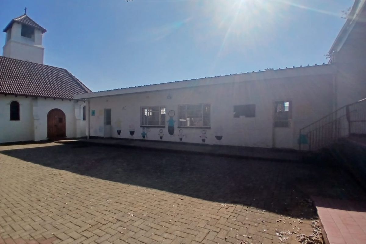 Exterior view of a commercial property courtyard featuring paved surfaces, a tiled roof structure, and adjacent building facade with casement windows.