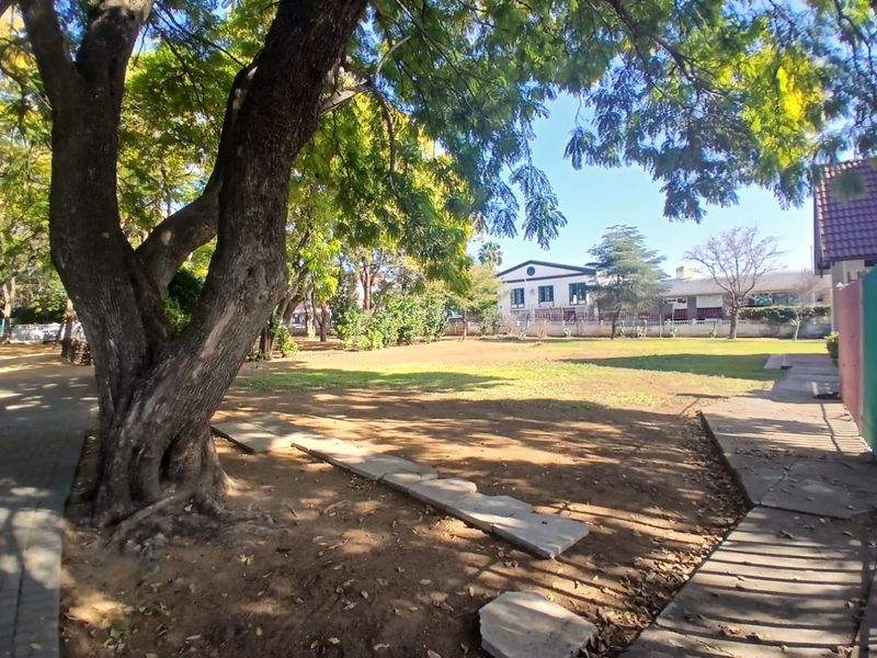 A spacious outdoor garden area featuring mature trees, a paved walkway, and established boundary walls, offering potential for landscaping improvements.