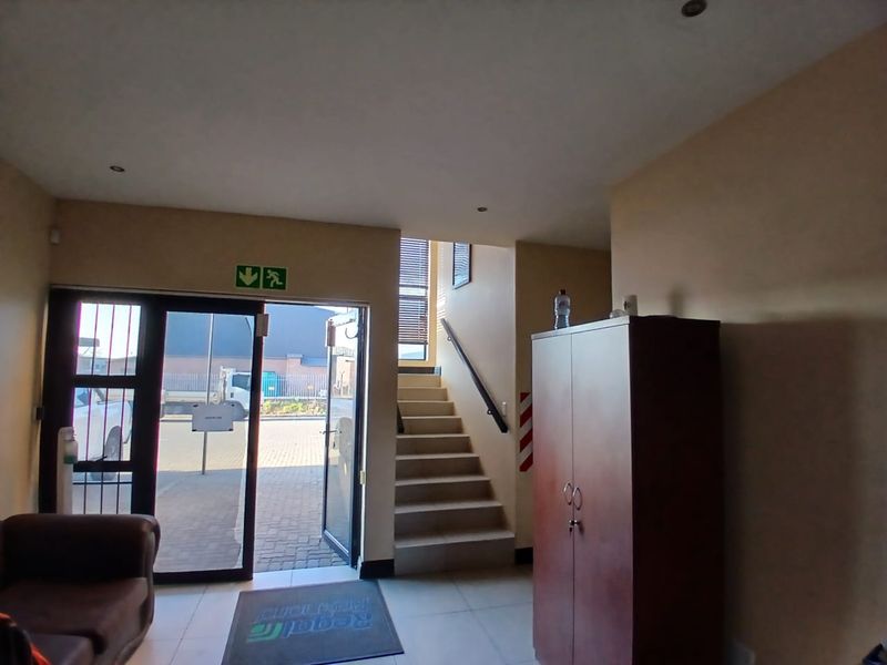 Industrial property entrance area featuring tiled flooring, a staircase with a handrail, and direct access to the exterior through a security door.