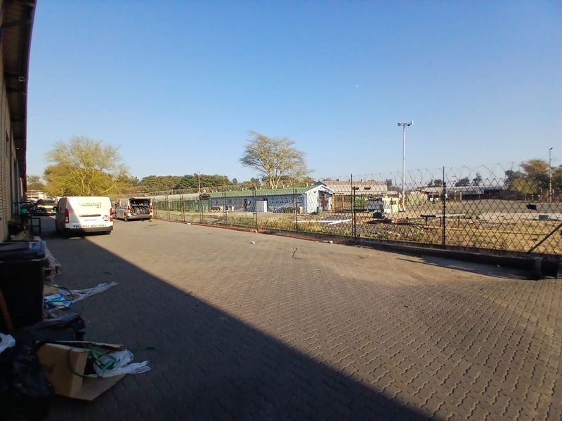 An industrial rear yard area featuring paved surfacing, perimeter chain link fencing with razor wire, and exterior site lighting.