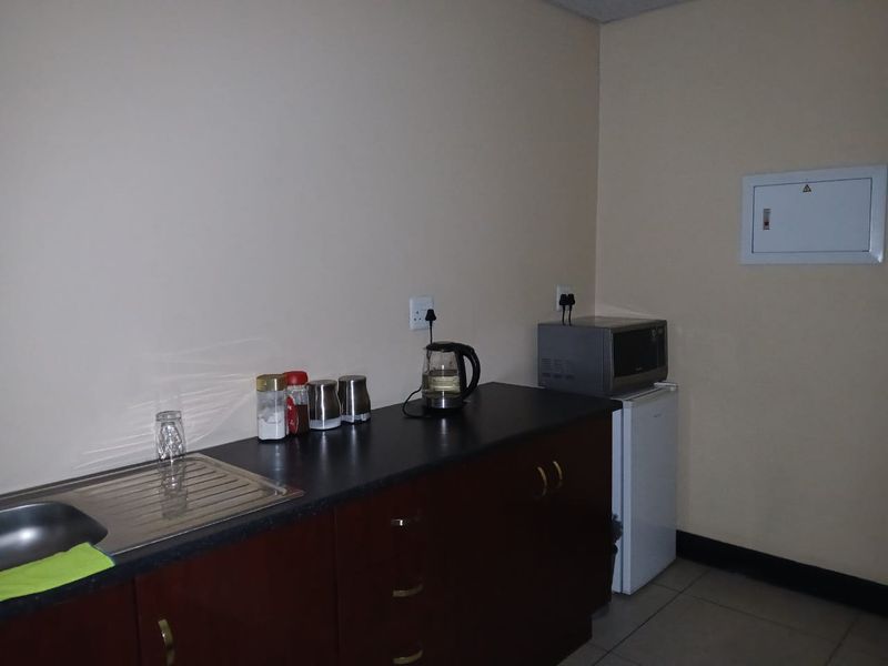 A compact kitchenette featuring dark wood cabinetry, a laminate countertop with an integrated stainless steel sink, and a wall-mounted electrical distribution board.