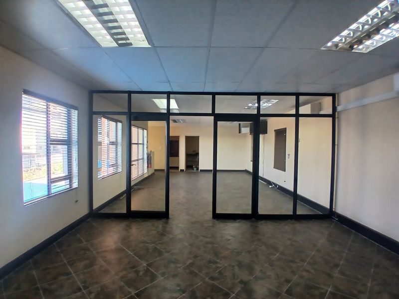 Spacious open-plan office area featuring modern aluminium-framed glass partitioning, suspended ceilings with integrated lighting, and durable tiled flooring.