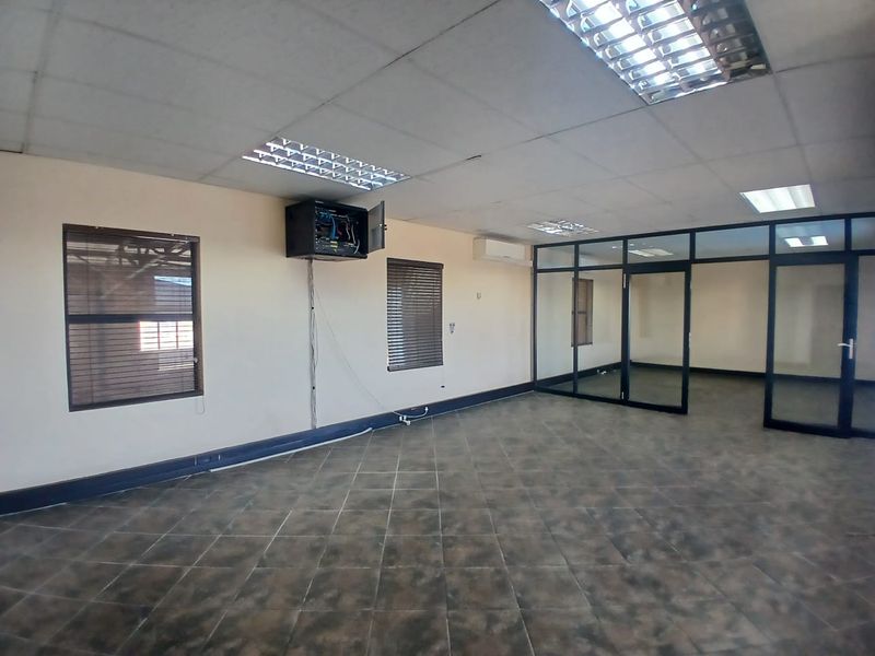 Open-plan office space featuring tiled flooring, suspended ceilings with recessed lighting, glass partitioning, and wall-mounted air conditioning.