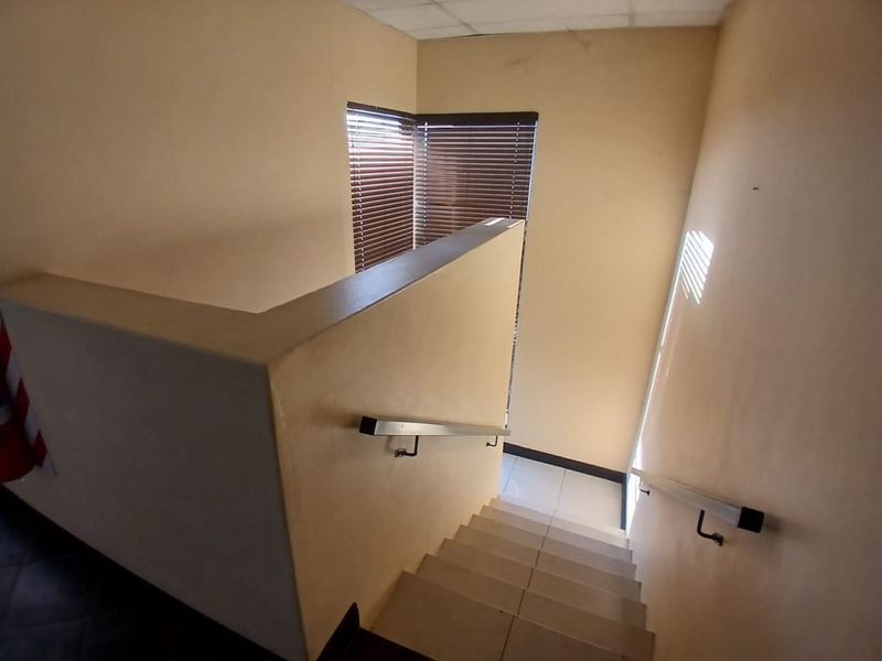 A functional industrial staircase area featuring tiled steps, metal handrails, and venetian blinds, providing access between levels.