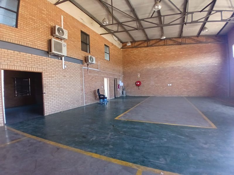 Spacious industrial utility area featuring exposed steel roof trusses, face brick walls, and durable painted concrete flooring with wall-mounted air conditioning units.