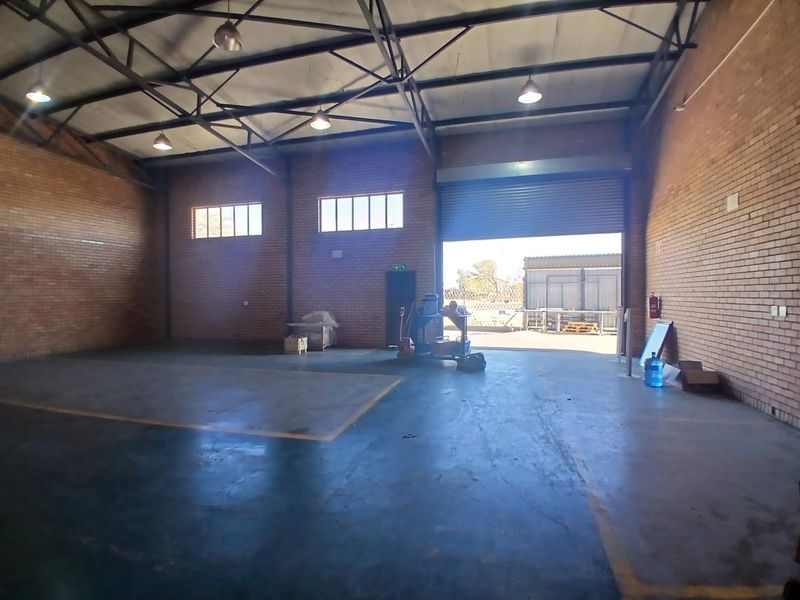Spacious industrial warehouse unit featuring exposed steel roof trusses, durable concrete flooring, face brick walls, and a large roller shutter door for easy access.