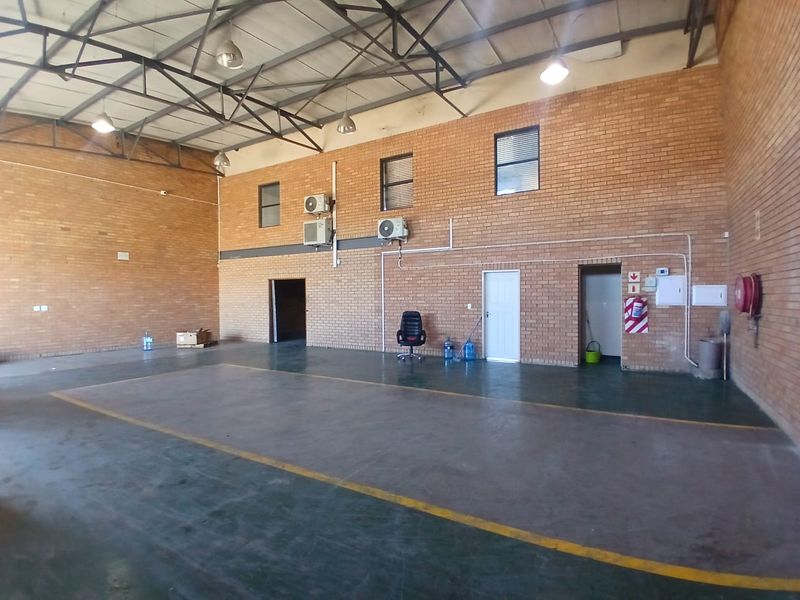 Spacious industrial utility area featuring exposed steel roof trusses, brick walls, concrete flooring, and wall-mounted air conditioning units.