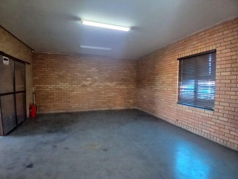 Spacious industrial garage featuring exposed brick walls, concrete flooring, and functional fluorescent lighting, suitable for storage or workshop use.