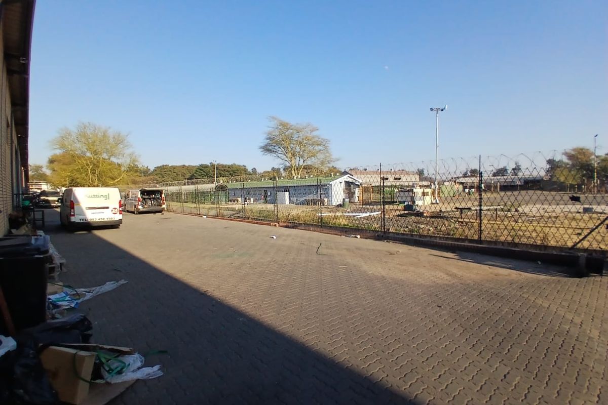 An industrial rear yard area featuring paved surfacing, perimeter chain link fencing with razor wire, and exterior site lighting.