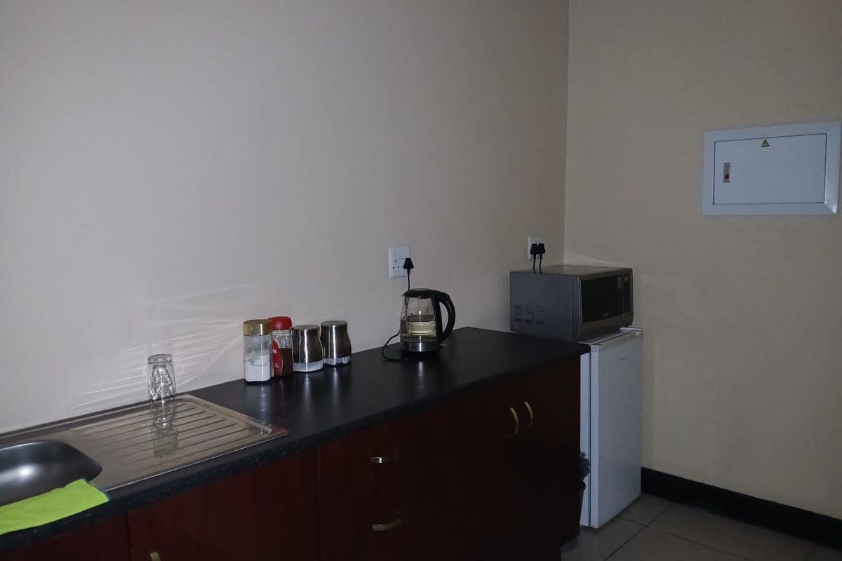 A compact kitchenette featuring dark wood cabinetry, a laminate countertop with an integrated stainless steel sink, and a wall-mounted electrical distribution board.
