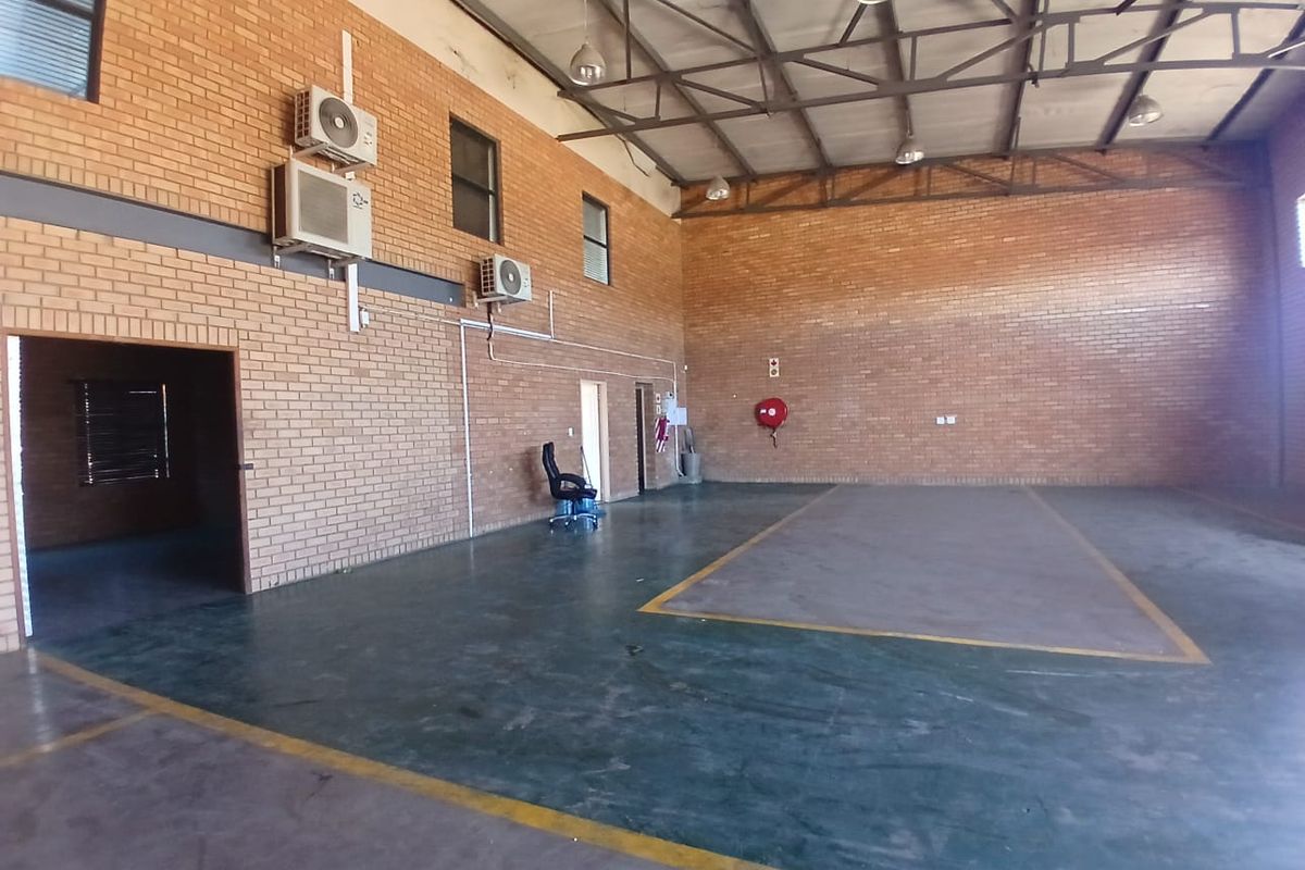 Spacious industrial utility area featuring exposed steel roof trusses, face brick walls, and durable painted concrete flooring with wall-mounted air conditioning units.
