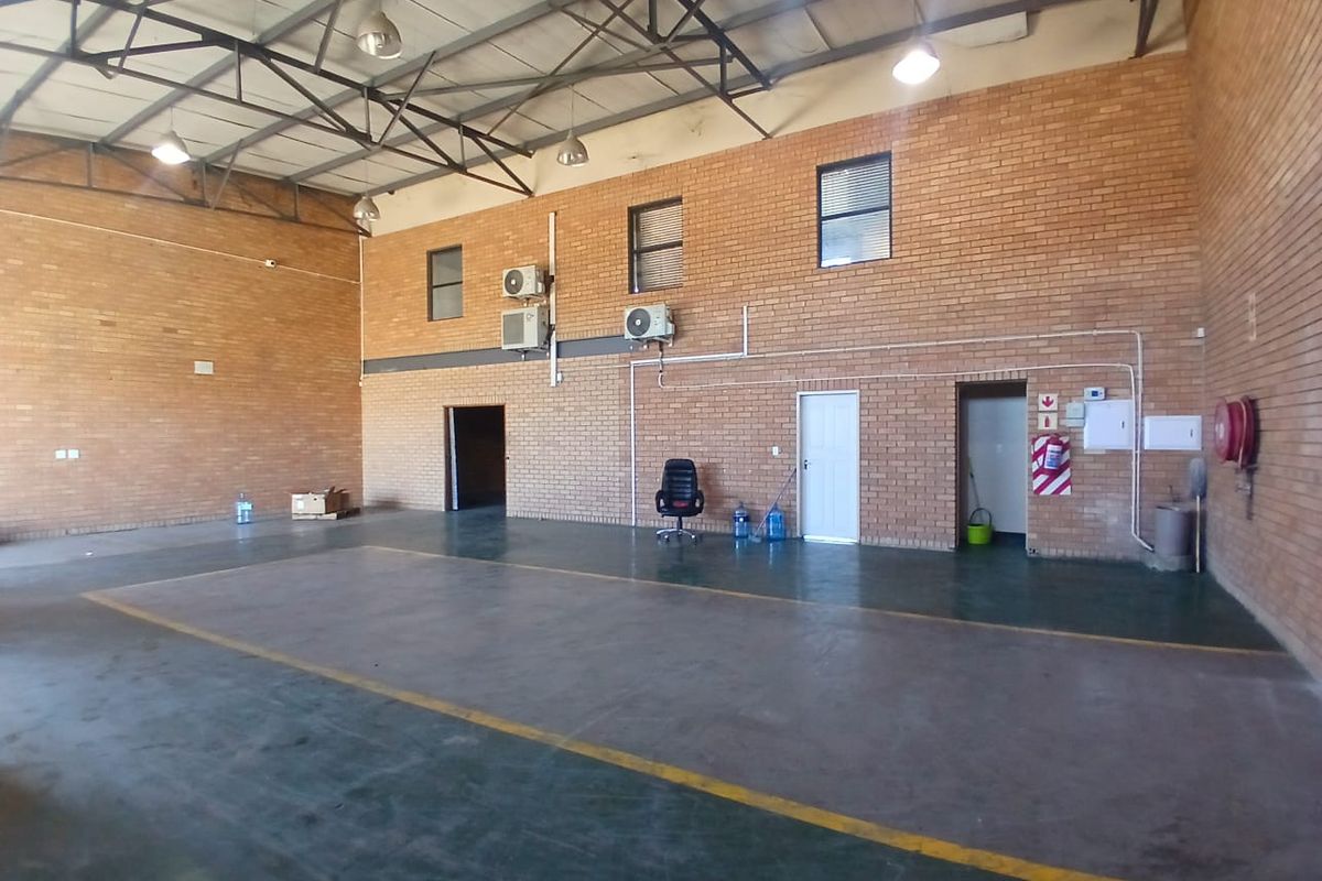 Spacious industrial utility area featuring exposed steel roof trusses, brick walls, concrete flooring, and wall-mounted air conditioning units.