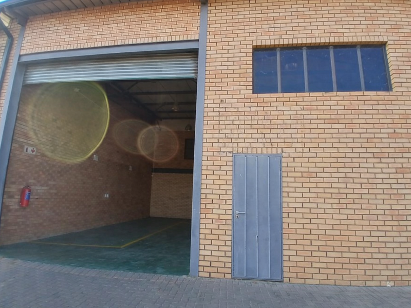 Industrial unit exterior featuring a large roller shutter door, pedestrian access door, and brick facade with high-level window.