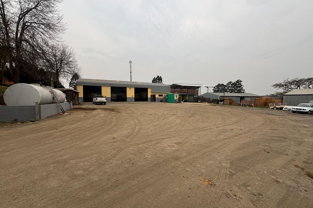 Industrial property featuring a large warehouse building with roller shutter doors, a fuel storage tank, and an expansive unpaved yard area.
