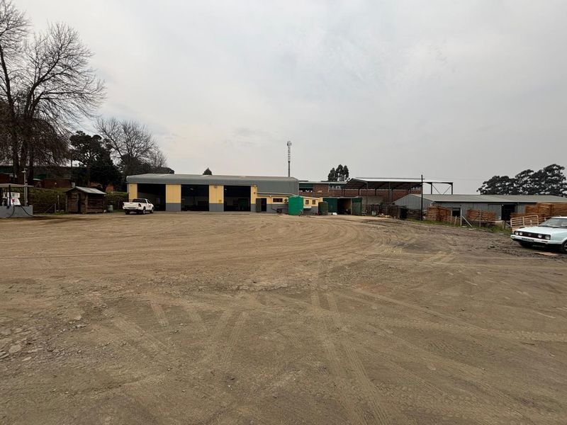 Wide-angle view of an industrial property featuring multiple warehouse bays, a large unpaved yard area, and surrounding perimeter fencing.