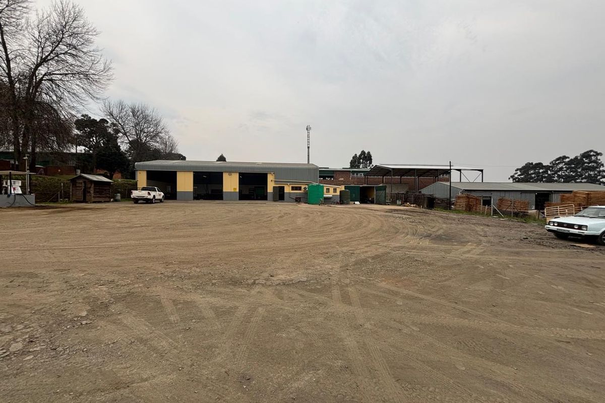 Wide-angle view of an industrial property featuring multiple warehouse bays, a large unpaved yard area, and surrounding perimeter fencing.
