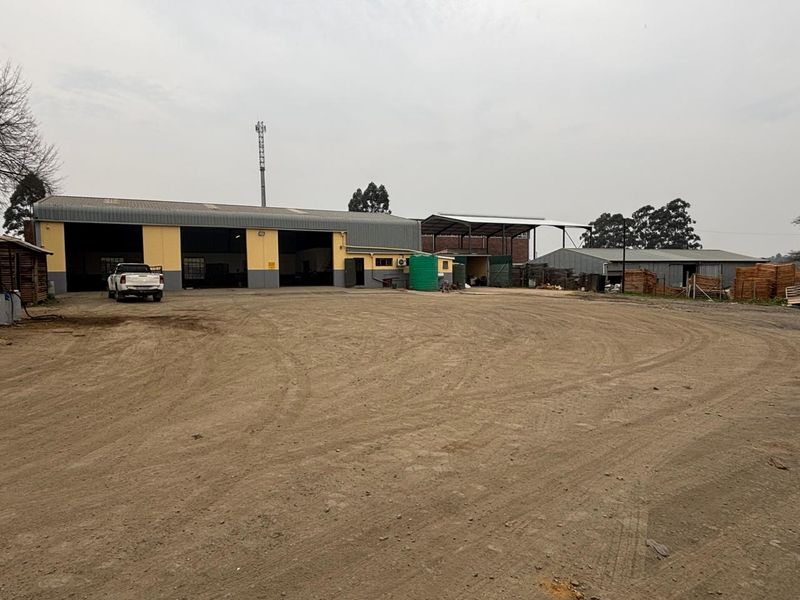 Industrial property featuring large warehouse structures with roller shutter doors and a spacious unpaved yard area.