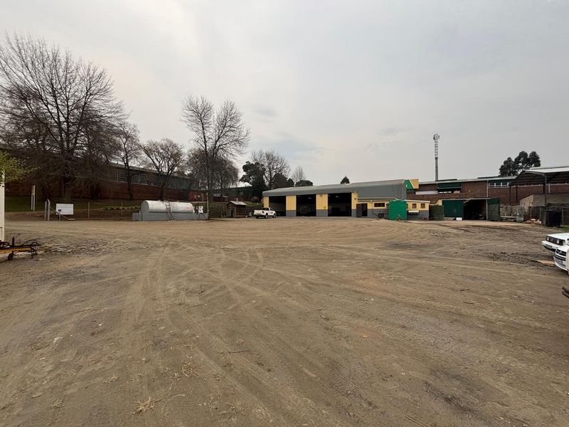 Industrial property featuring a large gravel yard, warehouse building with multiple roller shutter doors, and an on-site fuel storage tank.