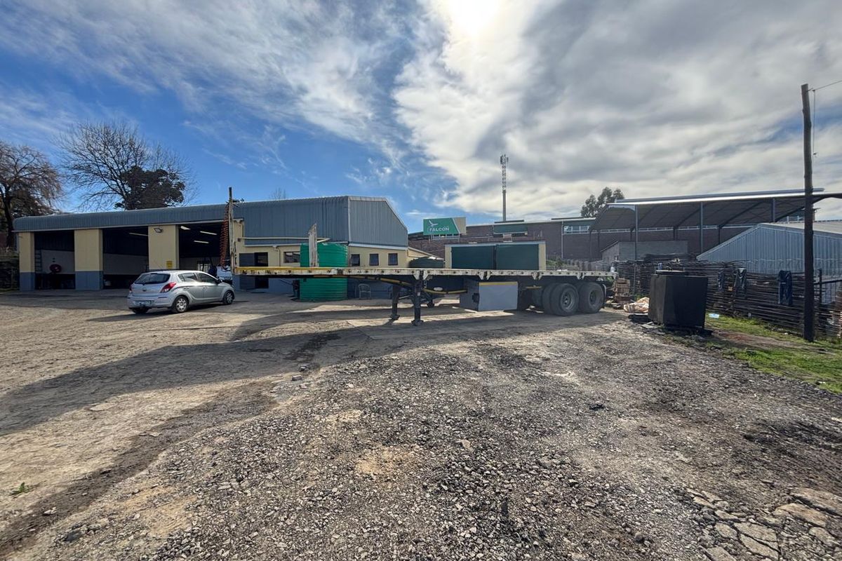 Industrial property featuring a large warehouse building with metal cladding, roller shutter doors, and an expansive gravel yard area for vehicle access.