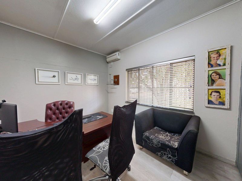 A functional office space featuring a split-system air conditioner, venetian blinds, and overhead fluorescent lighting, suitable for a professional work environment.