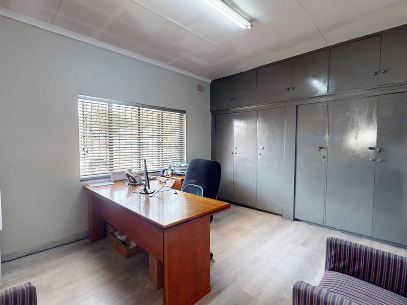 Functional office space featuring light laminate flooring, ample built-in storage cupboards, and natural light through venetian blinds.
