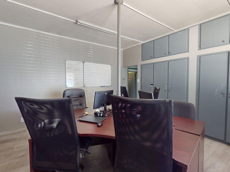 A functional office space featuring built-in storage cabinetry, laminate flooring, and overhead lighting, suitable for a professional work environment.