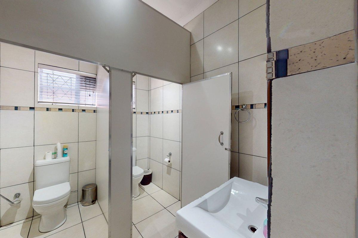 A functional office bathroom featuring tiled walls and floors, dual toilet cubicles with partition walls, and a wall-mounted washbasin.