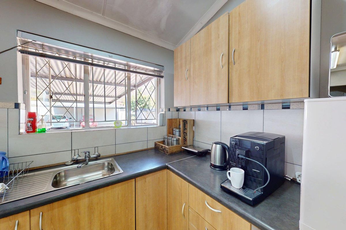 A functional kitchen featuring light wood-finish cabinetry, dark laminate countertops, a stainless steel sink, and a tiled backsplash with security bars on the window.