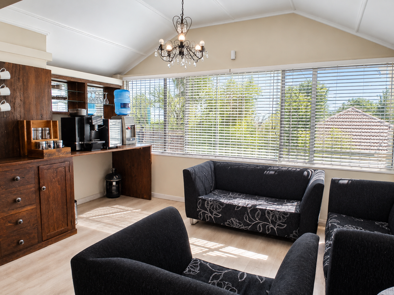 A bright office break area featuring built-in wooden cabinetry, a vaulted ceiling, and large windows with venetian blinds, creating a functional and inviting workspace.