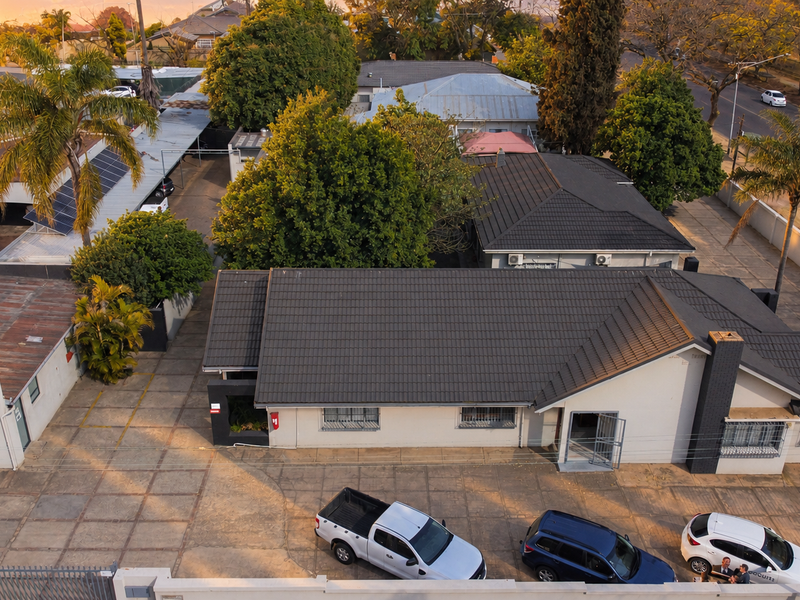 Aerial view of an office property featuring multiple buildings, tiled roofing, solar panels, and a paved parking area with perimeter security.