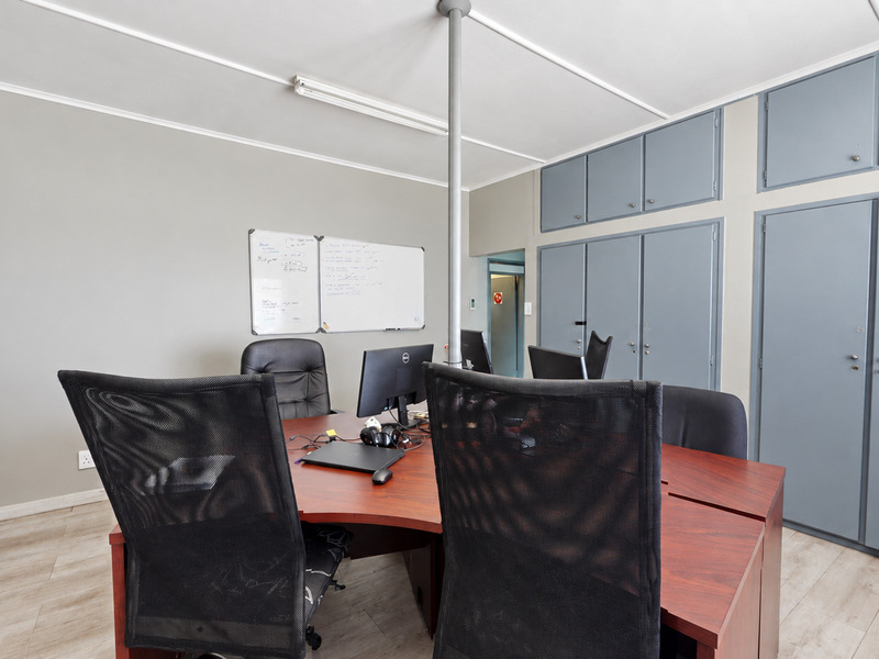 A functional office space featuring laminate flooring, extensive built-in storage cupboards, and a central support column.