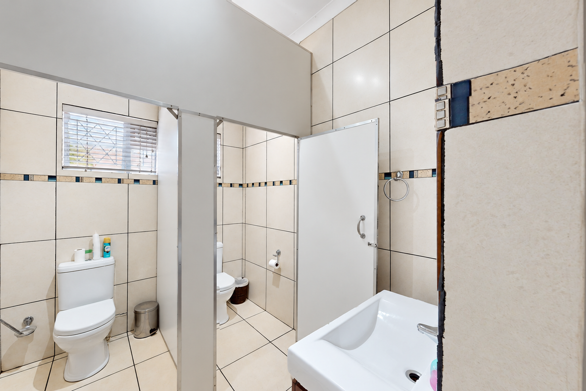 A functional office bathroom featuring tiled walls and floors, partitioned toilet cubicles, and a wall-mounted washbasin.