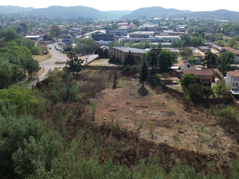 An aerial view of a vacant commercial plot of land situated in a developed urban area with surrounding infrastructure and greenery.