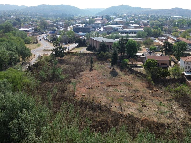 An aerial view of a vacant commercial land plot situated in a developed urban area with surrounding infrastructure and greenery.