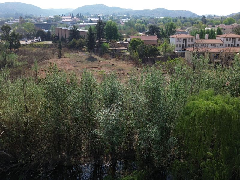 Aerial view of a vacant commercial land plot featuring mature trees and proximity to a waterway and urban infrastructure.