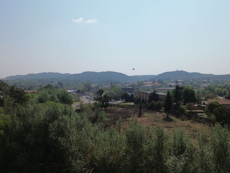 An elevated landscape view overlooking the surrounding area, featuring mature trees, vegetation, and distant hills.