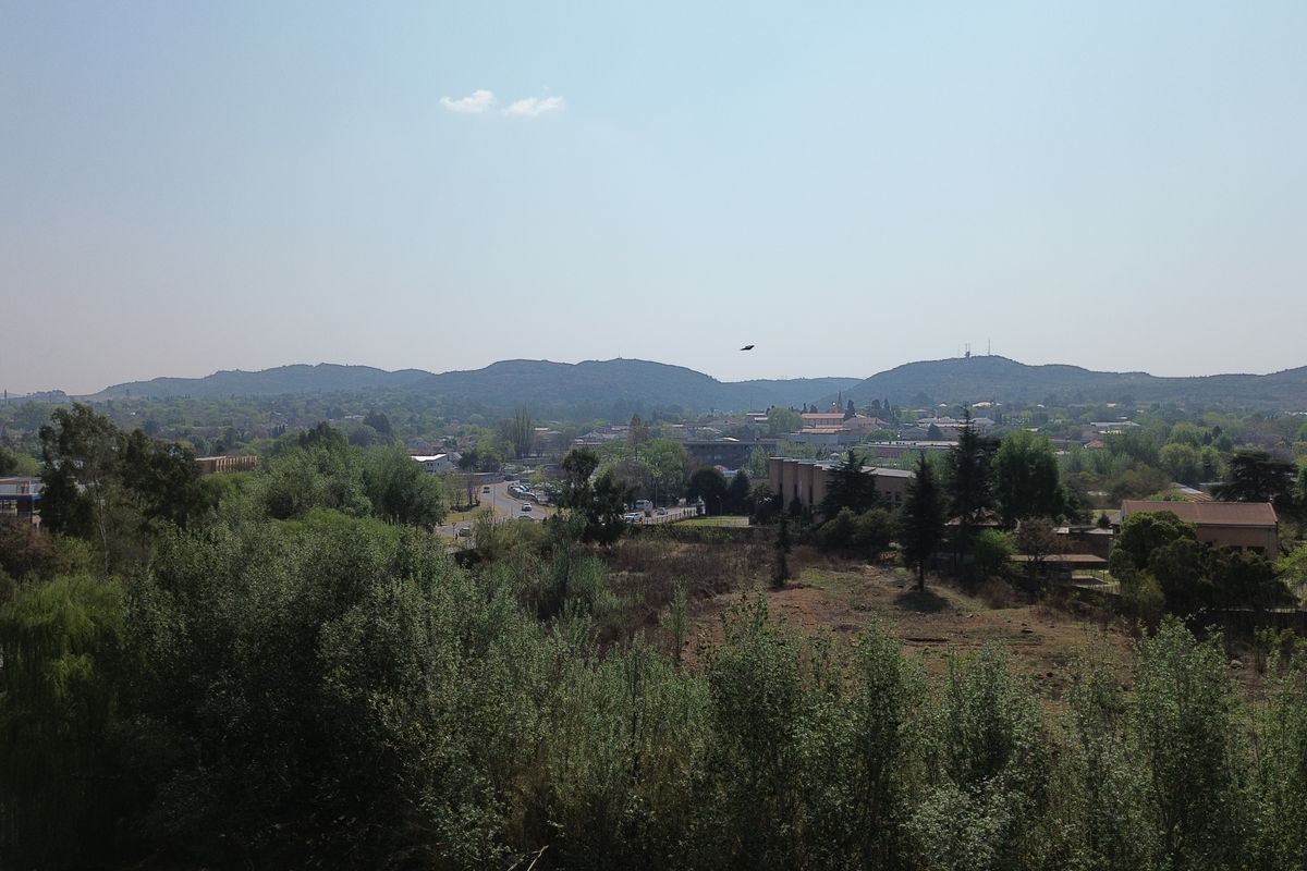 An elevated landscape view overlooking the surrounding area, featuring mature trees, vegetation, and distant hills.