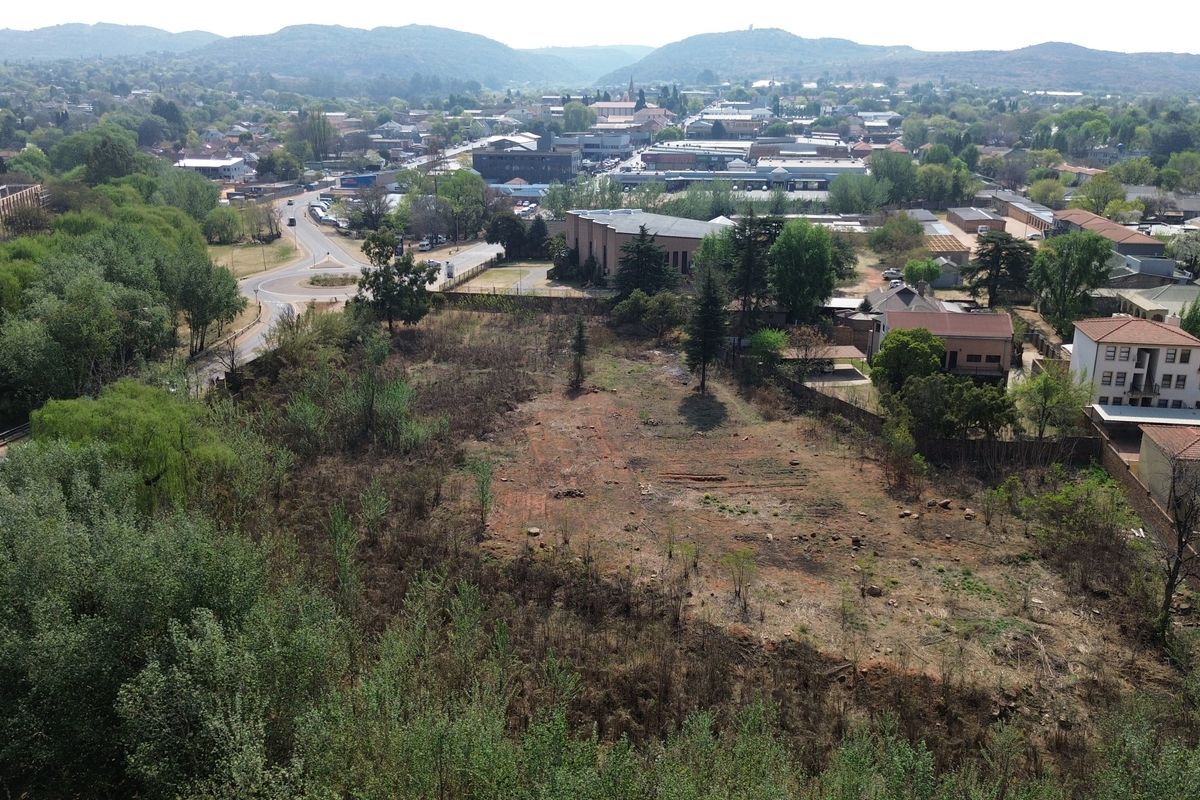An aerial view of a vacant commercial land plot situated in a developed urban area with surrounding infrastructure and greenery.