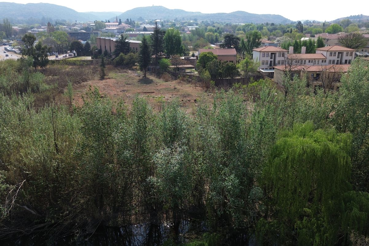 Aerial view of a vacant commercial land plot featuring mature trees and proximity to a waterway and urban infrastructure.