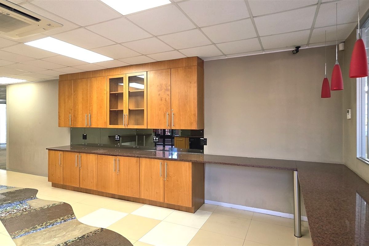 A clean, modern office kitchenette featuring wood-finish cabinetry, granite countertops, and a glass splashback, providing a functional break area for staff.