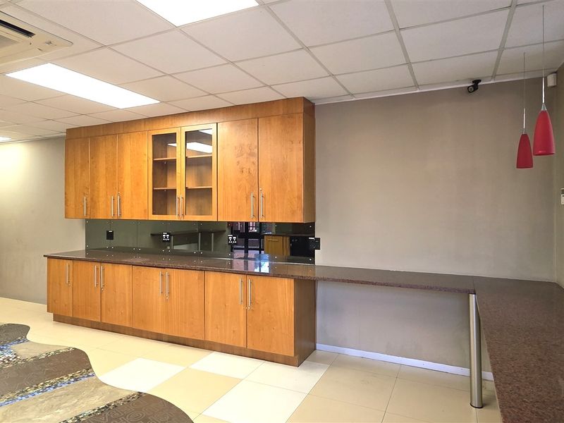 A clean, modern office kitchenette featuring wood-finish cabinetry, granite countertops, and a glass splashback, providing a functional break area for staff.