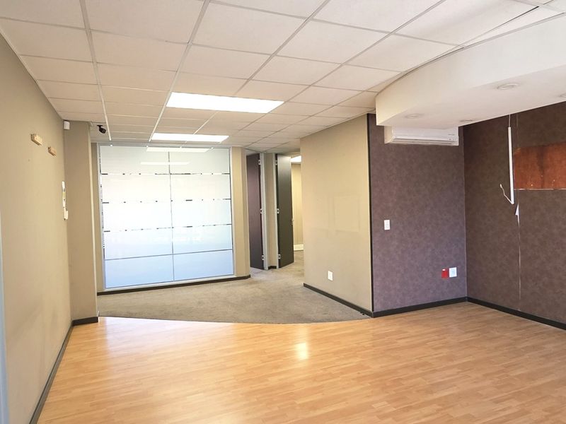 Empty office space featuring a mix of laminate and carpet flooring, suspended ceiling with recessed lighting, and a glass partition wall.