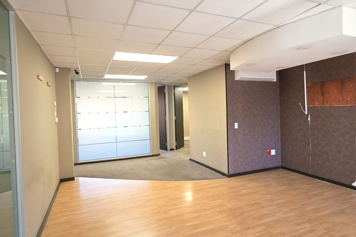 Empty office space featuring a mix of laminate and carpet flooring, suspended ceiling with recessed lighting, and a glass partition wall.