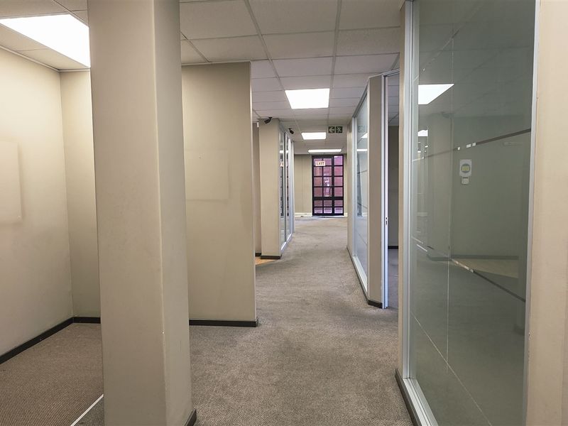 A vacant office hallway featuring suspended ceilings, recessed lighting, and glass partition walls, providing a clean and professional layout for a corporate environment.